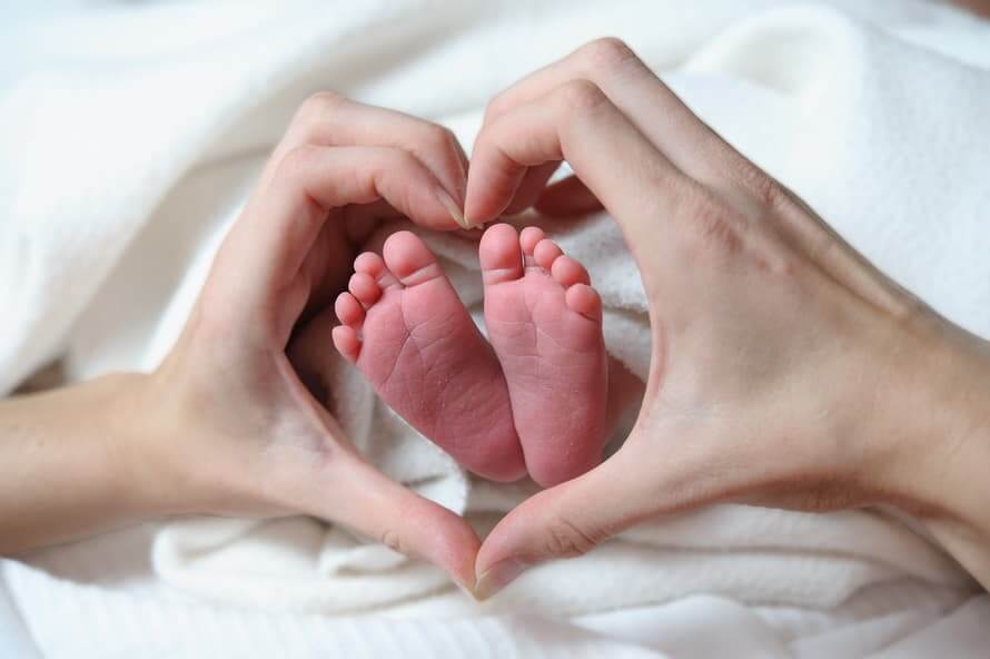 Hände formen ein Herz um zwei Babyfüße