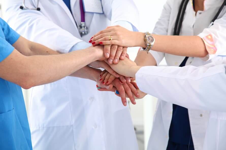 Ärzteteam verbindet die Hände in der Mitte als Zeichen von Zusammenhalt